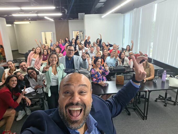 El equipo de NK Insurance celebrando con las manos en alto durante una capacitación en la oficina